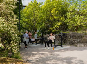 Människor tränar på ett utegym med stålmaskiner i en grönskande park.