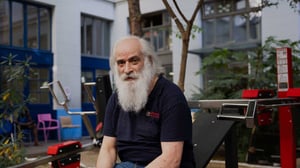 Senior man taking a break between repetitions while exercising on Omnigym outdoor gym equipment at an Emmaüs Solidarité shelter for people experiencing homelessness in Paris, France, highlighting accessible outdoor fitness facilities in a community support environment.